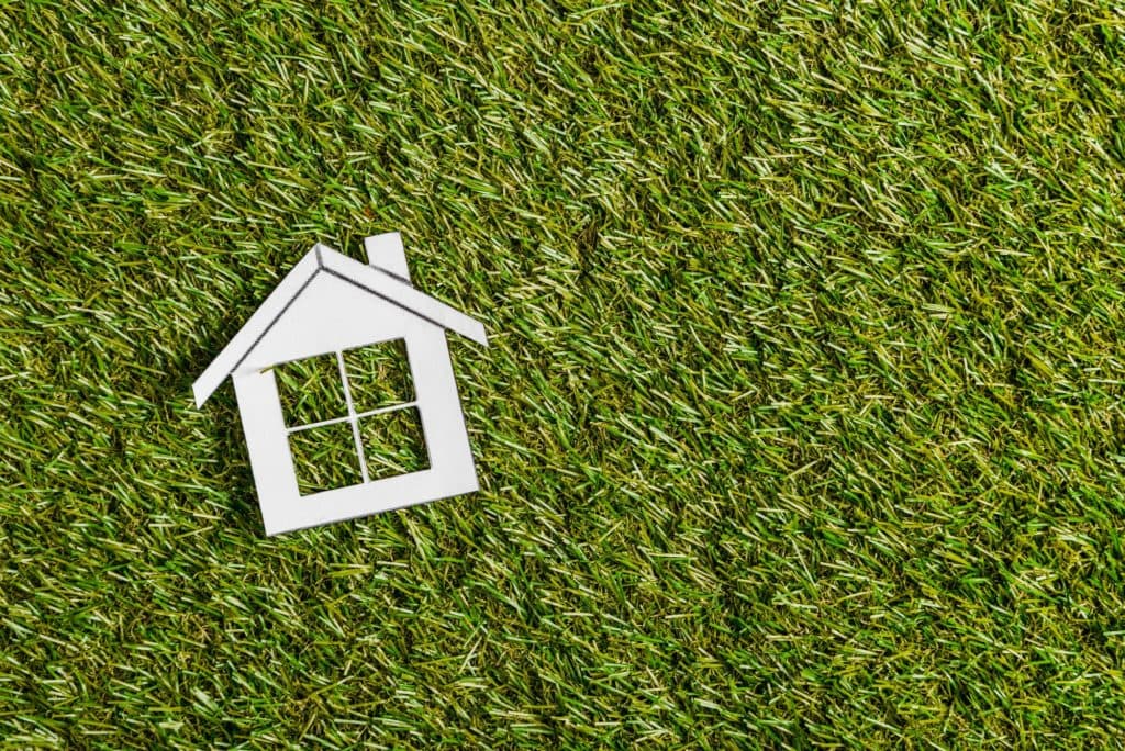Paper house on green grass representing home energy efficiency